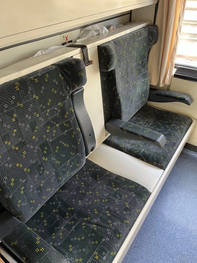 To grå sæder med armlæn i en togkupé