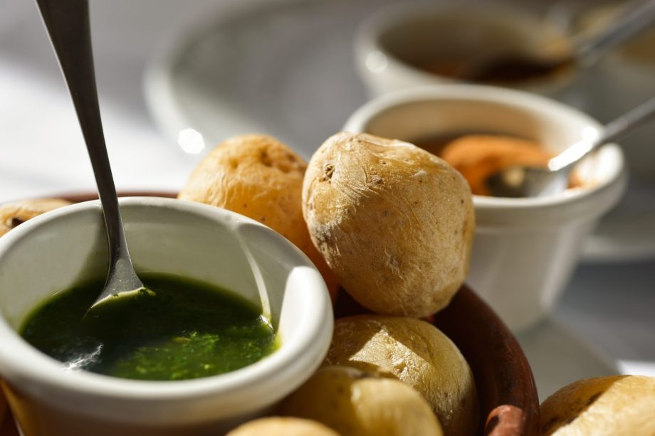 Kogte kartofler med skræl på et brun fad med en hvid skål med grøn pesto ved siden af