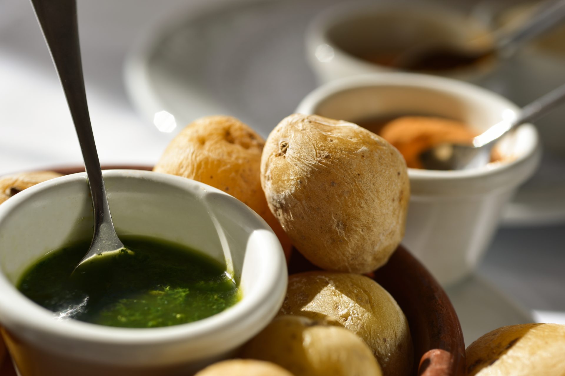 Kogte kartofler med skræl på et brun fad med en hvid skål med grøn pesto ved siden af