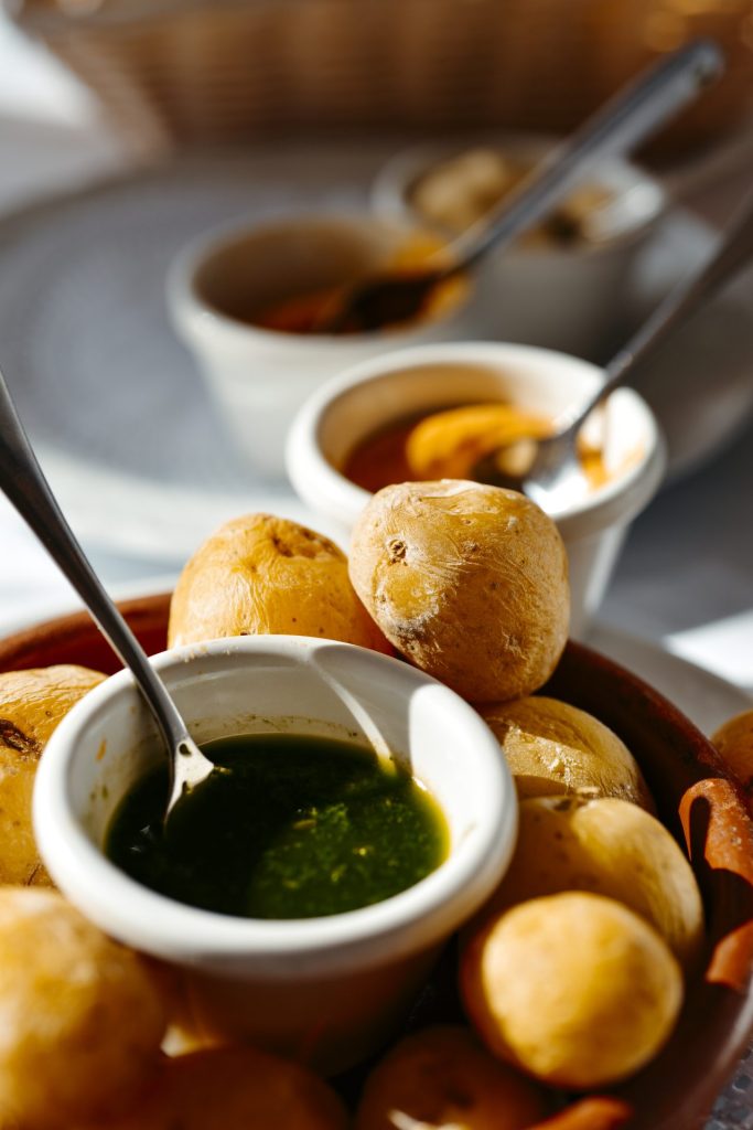 Kogte kartofler med skræl i en brun skål med en lille hvid skål med grøn pesto og en ske i