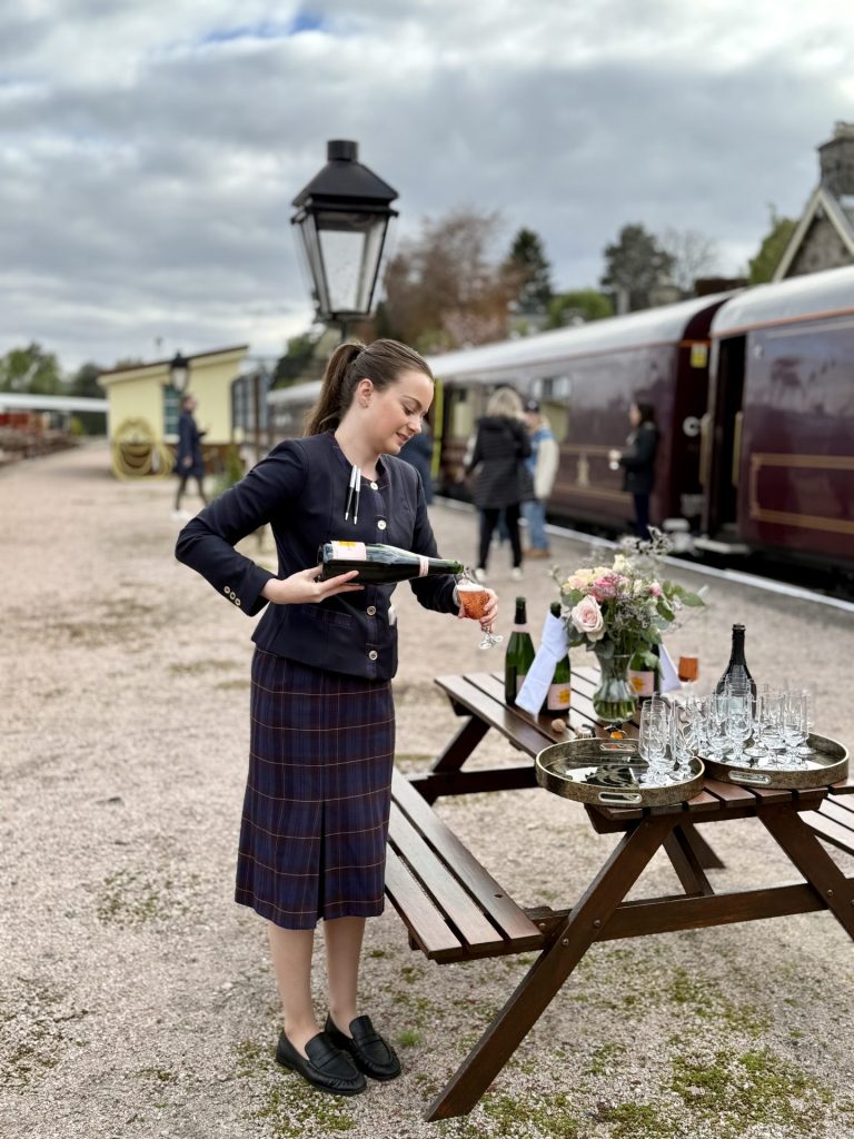 En kvinde der serverer rosé i et glas ved siden af et bordebænkesæt med flere vinglas på